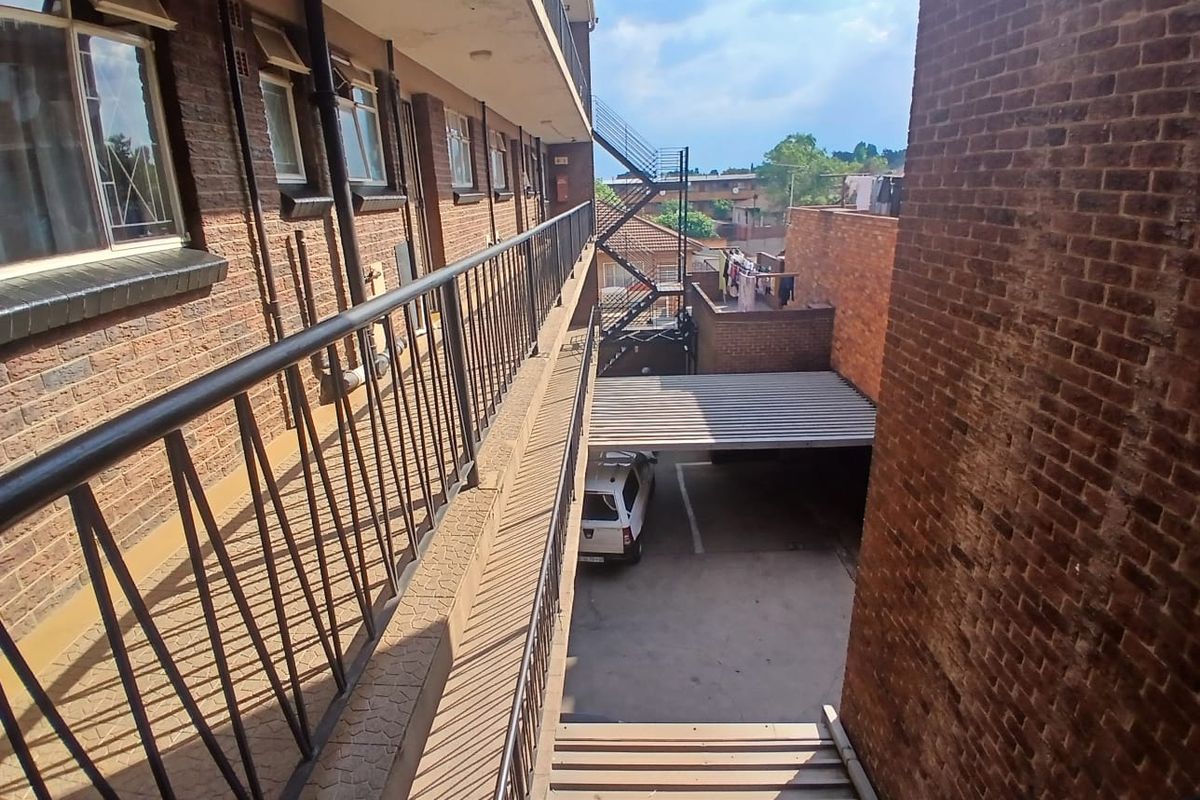 View of the townhouse exterior walkway, featuring brick facade, metal balustrades, and an external staircase leading to the ground level parking area.
