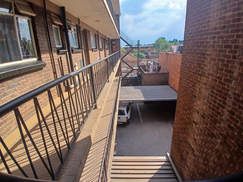 View of the townhouse exterior walkway, featuring brick facade, metal balustrades, and an external staircase leading to the ground level parking area.