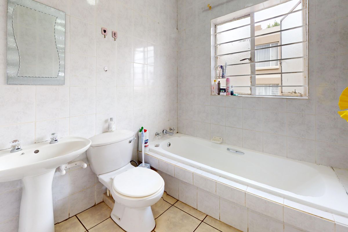 A functional bathroom featuring a pedestal basin, toilet, and built-in bathtub with full-height wall tiling and security bars on the window.
