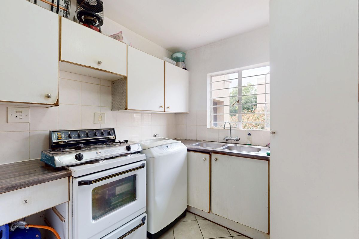 Compact kitchen featuring white cabinetry, tiled splashbacks, a double sink, and a window with security bars, offering a functional layout for renovation.