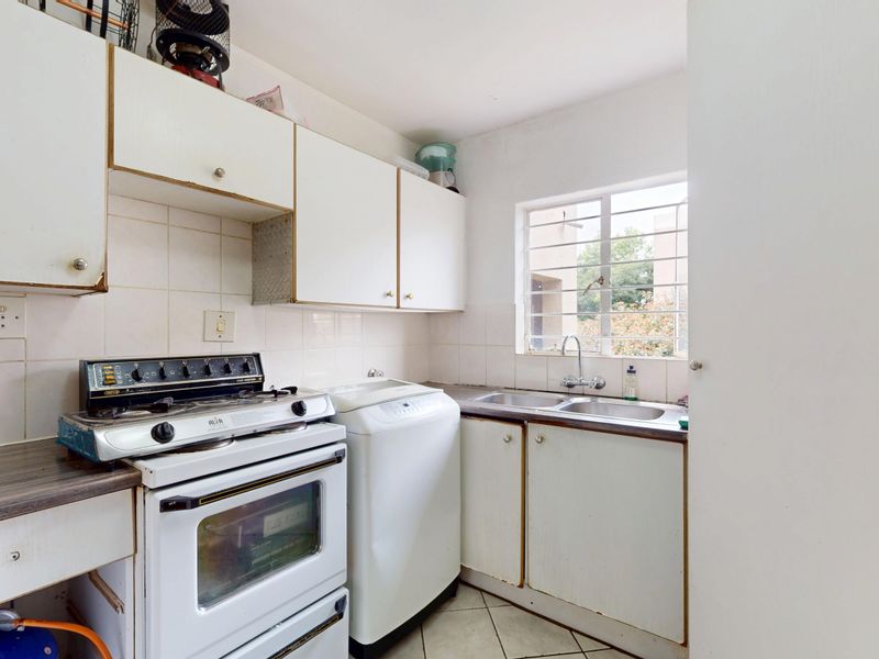 Compact kitchen featuring white cabinetry, tiled splashbacks, a double sink, and a window with security bars, offering a functional layout for renovation.