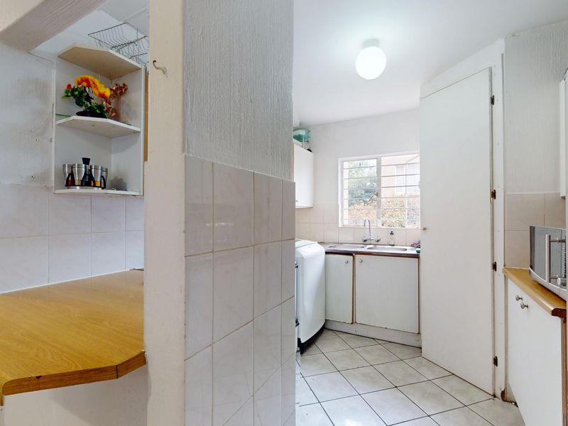 Functional kitchen area featuring tiled splashbacks, laminate countertops, built-in cabinetry, and a stainless steel sink with natural light from the window.