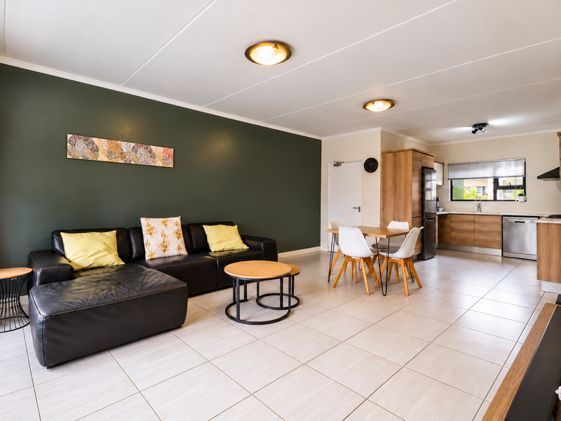 Spacious open-plan living and dining area featuring modern tiled flooring, a contemporary kitchen with wood-finish cabinetry, and a striking dark green feature wall.