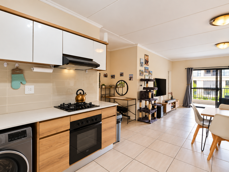 Modern open-plan kitchen and living area featuring sleek cabinetry, integrated appliances, tiled flooring, and direct access to a private balcony.