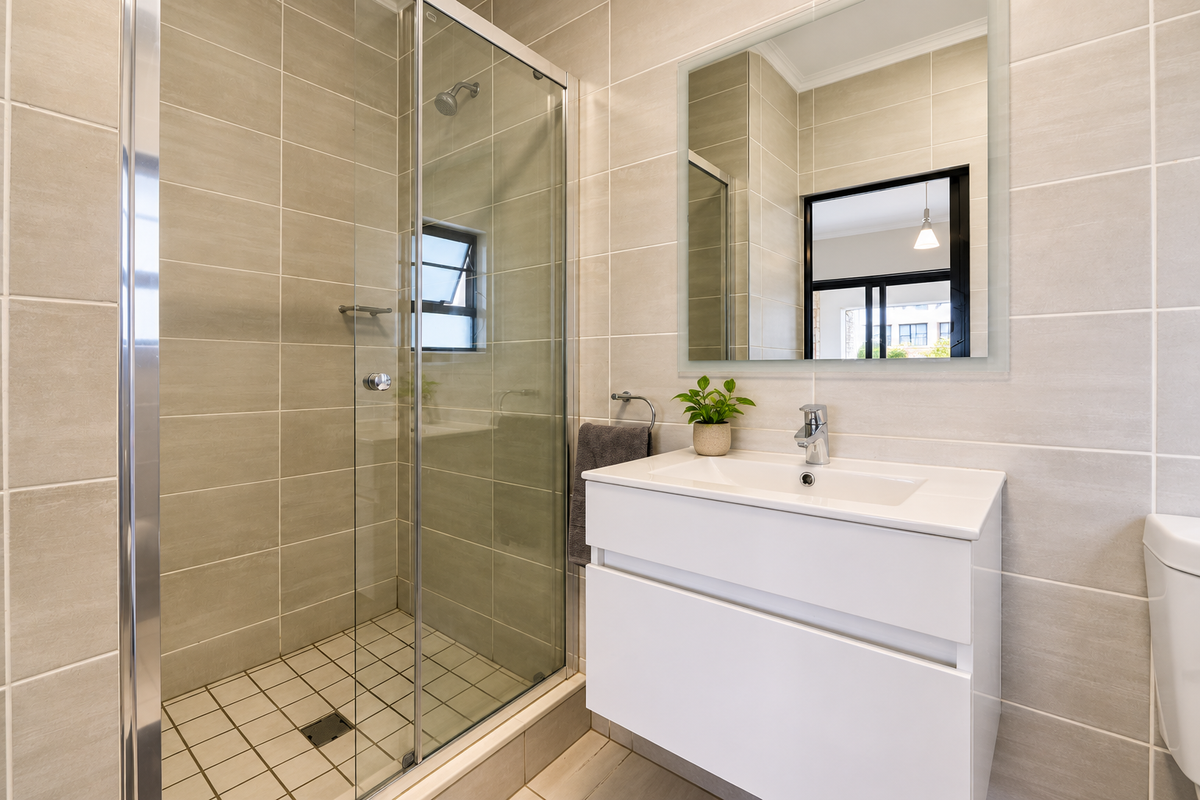 Modern bathroom featuring a glass-enclosed shower, wall-mounted vanity with basin, and neutral tiled finishes throughout.