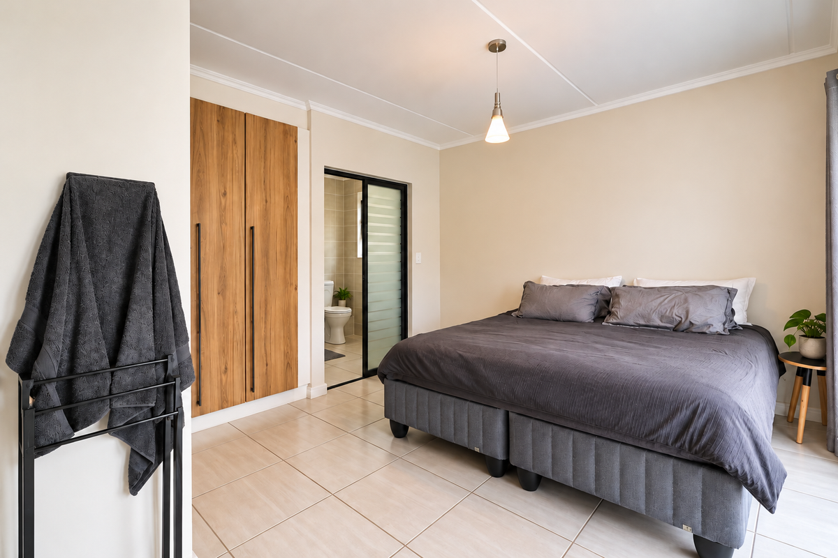 A well-maintained bedroom featuring tiled flooring, a built-in wooden wardrobe, and an en-suite bathroom accessible via a sliding door.