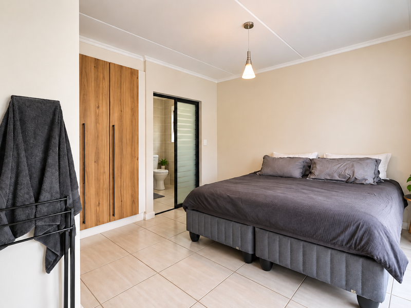 A well-maintained bedroom featuring tiled flooring, a built-in wooden wardrobe, and an en-suite bathroom accessible via a sliding door.