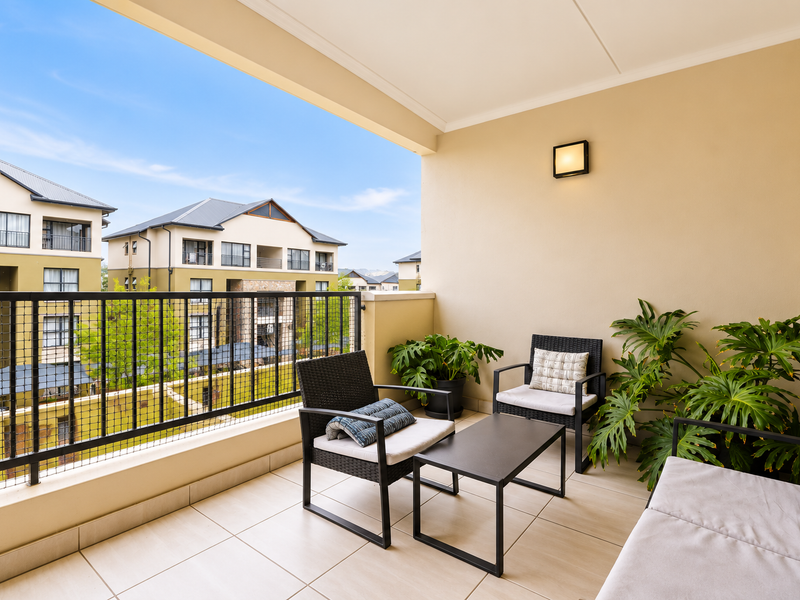A well-maintained covered balcony featuring tiled flooring and a secure metal balustrade, offering a pleasant outdoor space for relaxation.