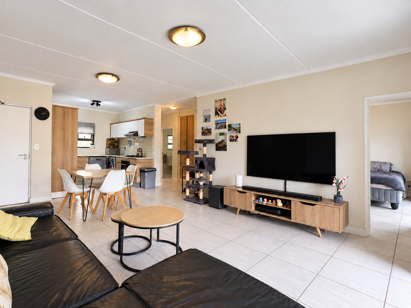 An open-plan living and kitchen area featuring neutral tiled flooring, modern cabinetry, and a functional layout connecting the lounge to the kitchen space.