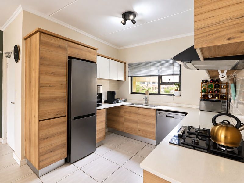 Modern kitchen featuring wood-finish cabinetry, stone countertops, a gas hob with extractor fan, and tiled flooring in a well-maintained, contemporary layout.