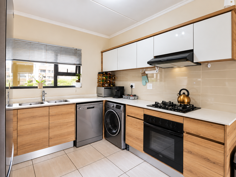 Modern kitchen featuring wood-grain cabinetry, white stone countertops, integrated gas hob, built-in oven, extractor fan, and tiled flooring with ample natural light.