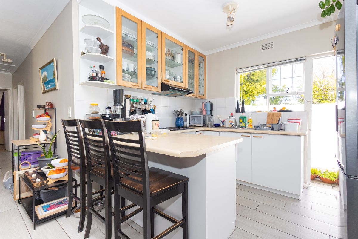 A functional kitchen featuring laminate countertops, ample built-in cabinetry with glass-fronted uppers, a tiled backsplash, and a breakfast bar area.