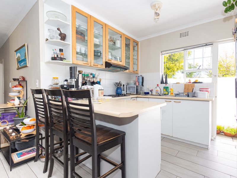 A functional kitchen featuring laminate countertops, ample built-in cabinetry with glass-fronted uppers, a tiled backsplash, and a breakfast bar area.