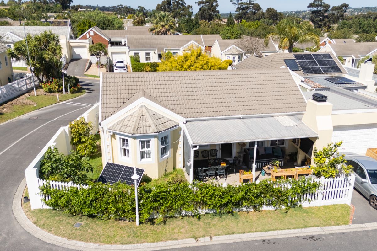 Aerial view of a townhouse featuring a tiled roof with solar panels, a covered patio area, and a private garden with picket fencing.