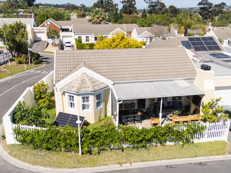 Aerial view of a townhouse featuring a tiled roof with solar panels, a covered patio area, and a private garden with picket fencing.