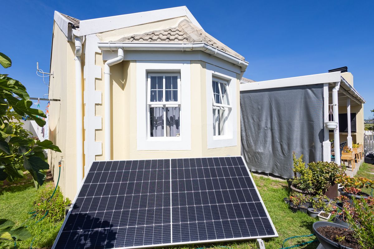 Rear exterior view of the townhouse featuring a tiled roof, sash windows, and a ground-mounted solar panel installation adjacent to a covered patio area.