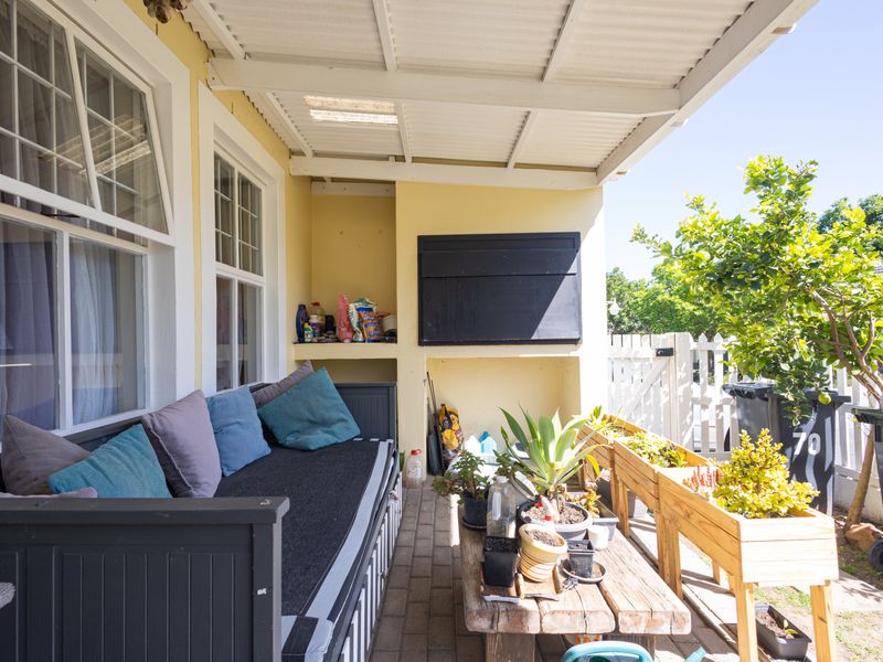 A covered patio area featuring paved flooring, built-in shelving, and a white picket fence, providing a functional outdoor space for relaxation.