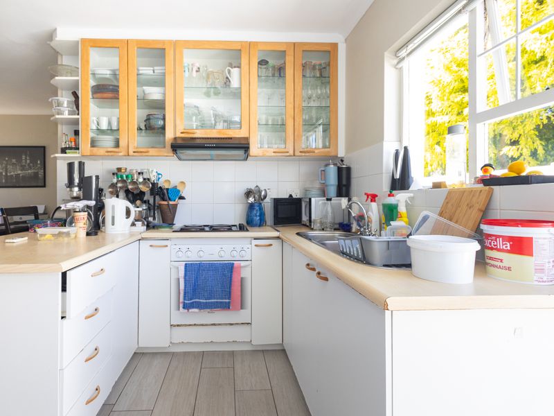 A functional kitchen featuring light wood-toned upper cabinetry, white base cabinets, laminate countertops, and a built-in oven with a gas hob.