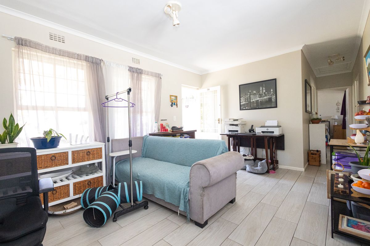 A bright living room featuring light-toned tiled flooring and neutral wall finishes, providing a versatile space for relaxation or home office use.