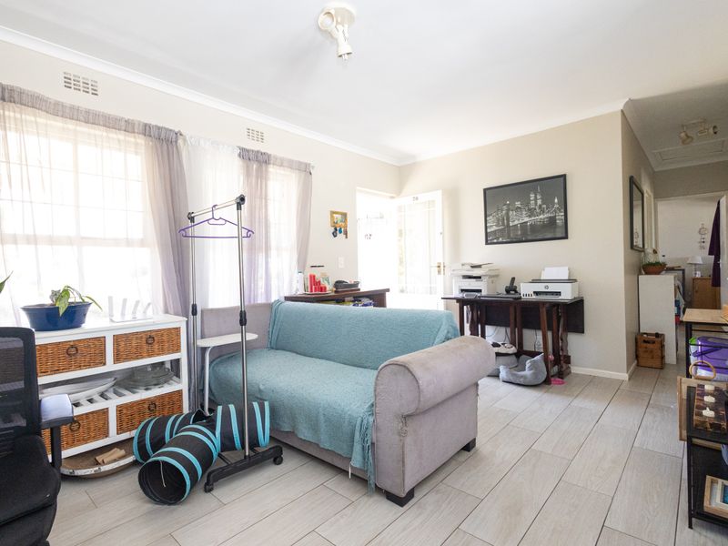 A bright living room featuring light-toned tiled flooring and neutral wall finishes, providing a versatile space for relaxation or home office use.