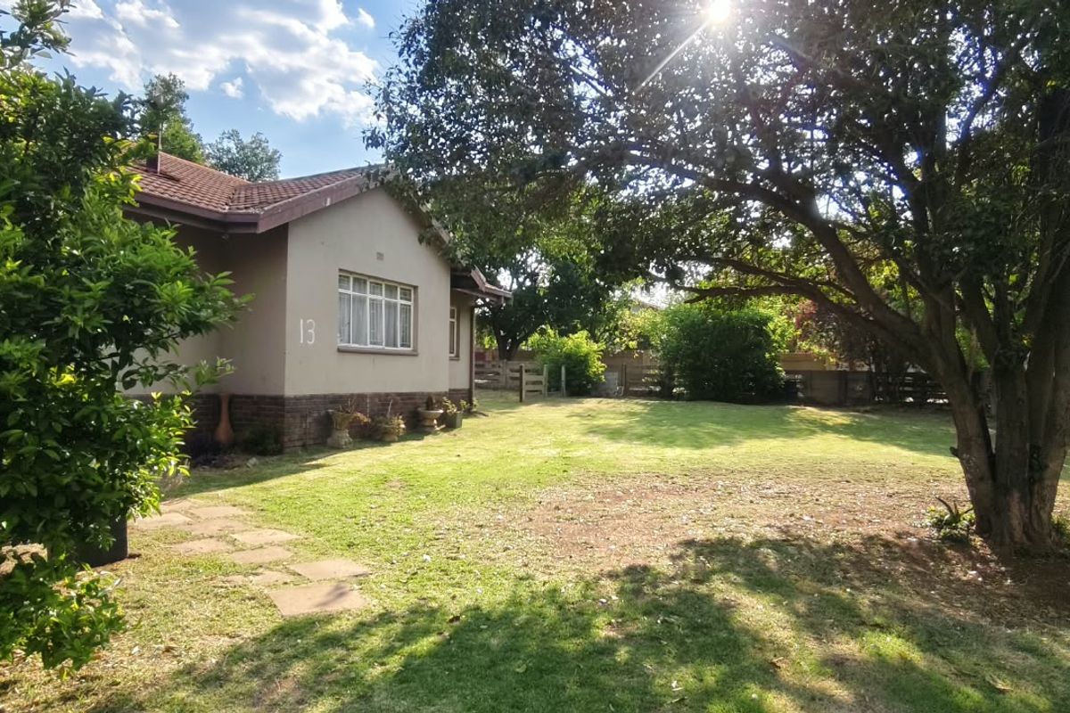 A view of the rear garden and side elevation of the house, featuring a tiled roof, brick facade, and established trees.