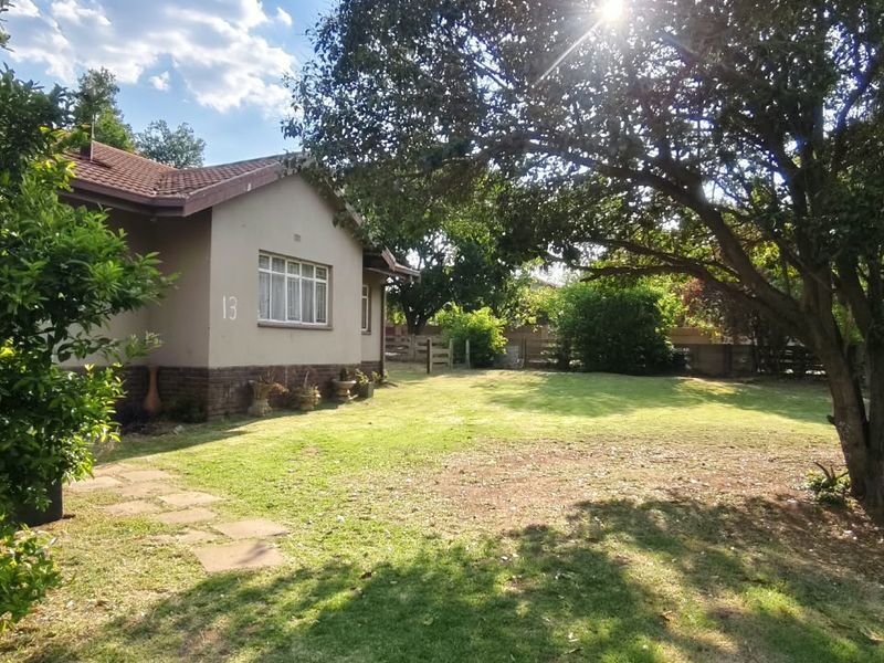 A view of the rear garden and side elevation of the house, featuring a tiled roof, brick facade, and established trees.