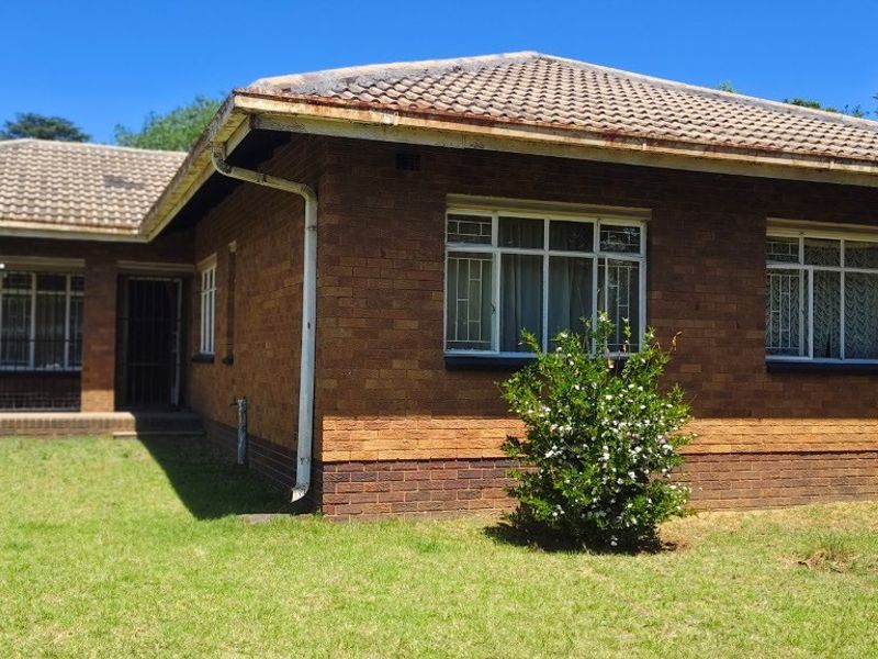 A single-story brick house featuring a tiled roof, security bars on windows, and a covered patio area set within a grassed garden.