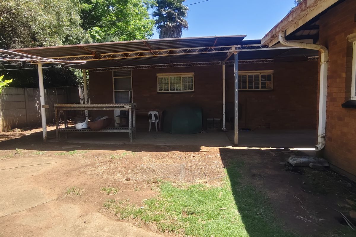 Rear exterior view featuring a covered patio area, brick facade, and a large backyard with potential for landscaping and outdoor living improvements.