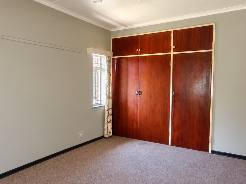 A spacious, empty bedroom featuring neutral wall tones, carpeted flooring, and ample built-in wooden storage cupboards.