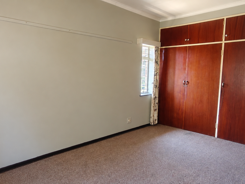 A vacant bedroom featuring built-in wooden cupboards, carpeted flooring, and a steel-framed window, offering a neutral canvas for potential updates.