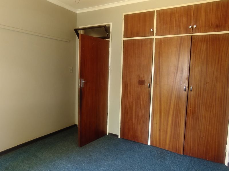 A vacant bedroom featuring built-in wooden cupboards and carpeted flooring, offering a blank canvas for potential updates and modernization.