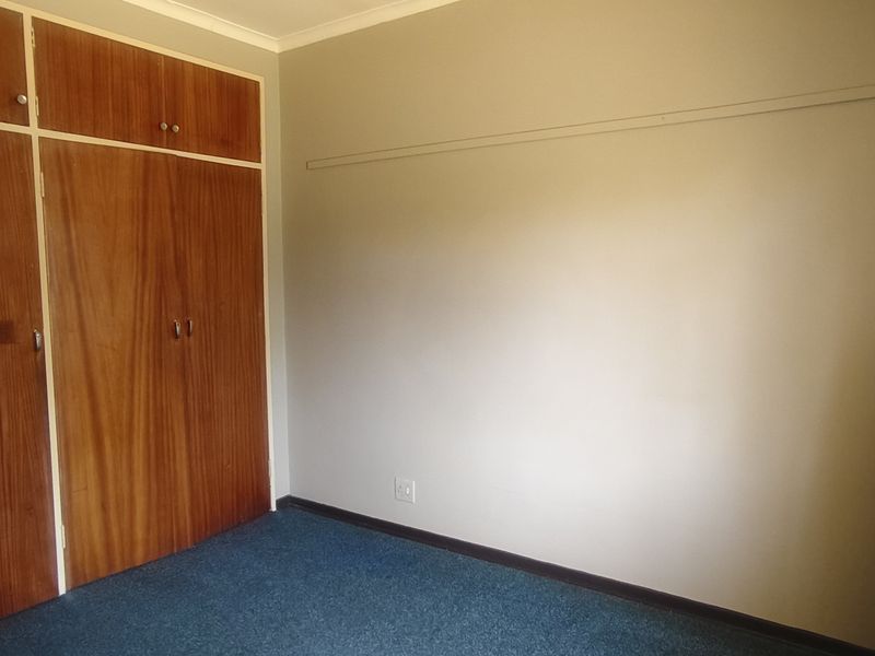 A bedroom featuring built-in wooden cupboards and carpeted flooring, offering a neutral space ready for personalization.