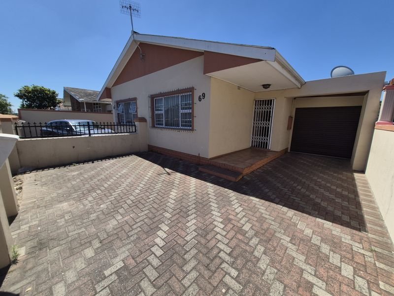 Front elevation of a townhouse featuring a paved driveway, single garage, and secure entrance with burglar bars and a boundary wall.