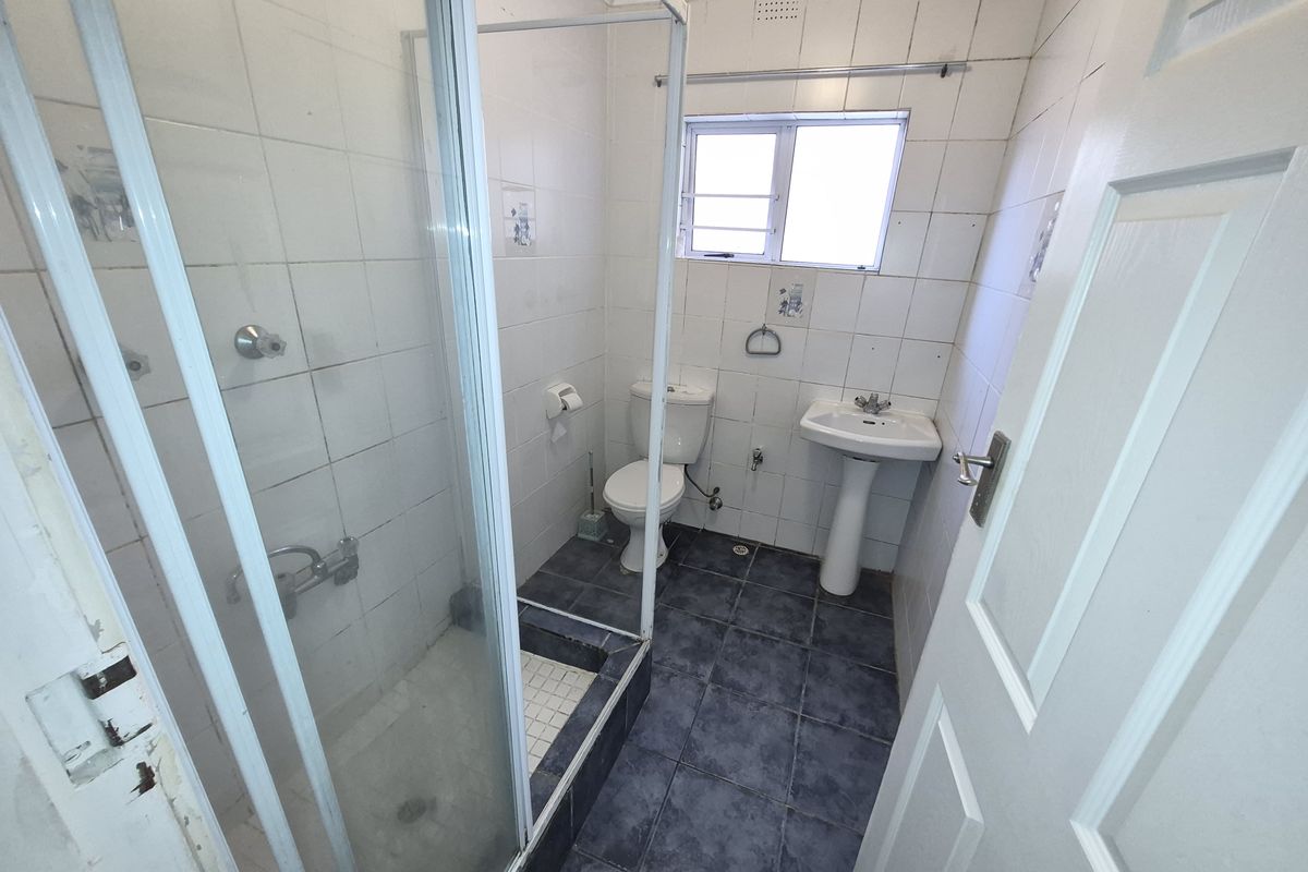 A compact bathroom featuring a shower enclosure, pedestal basin, and toilet, with tiled finishes throughout. The space requires cosmetic updates and maintenance.