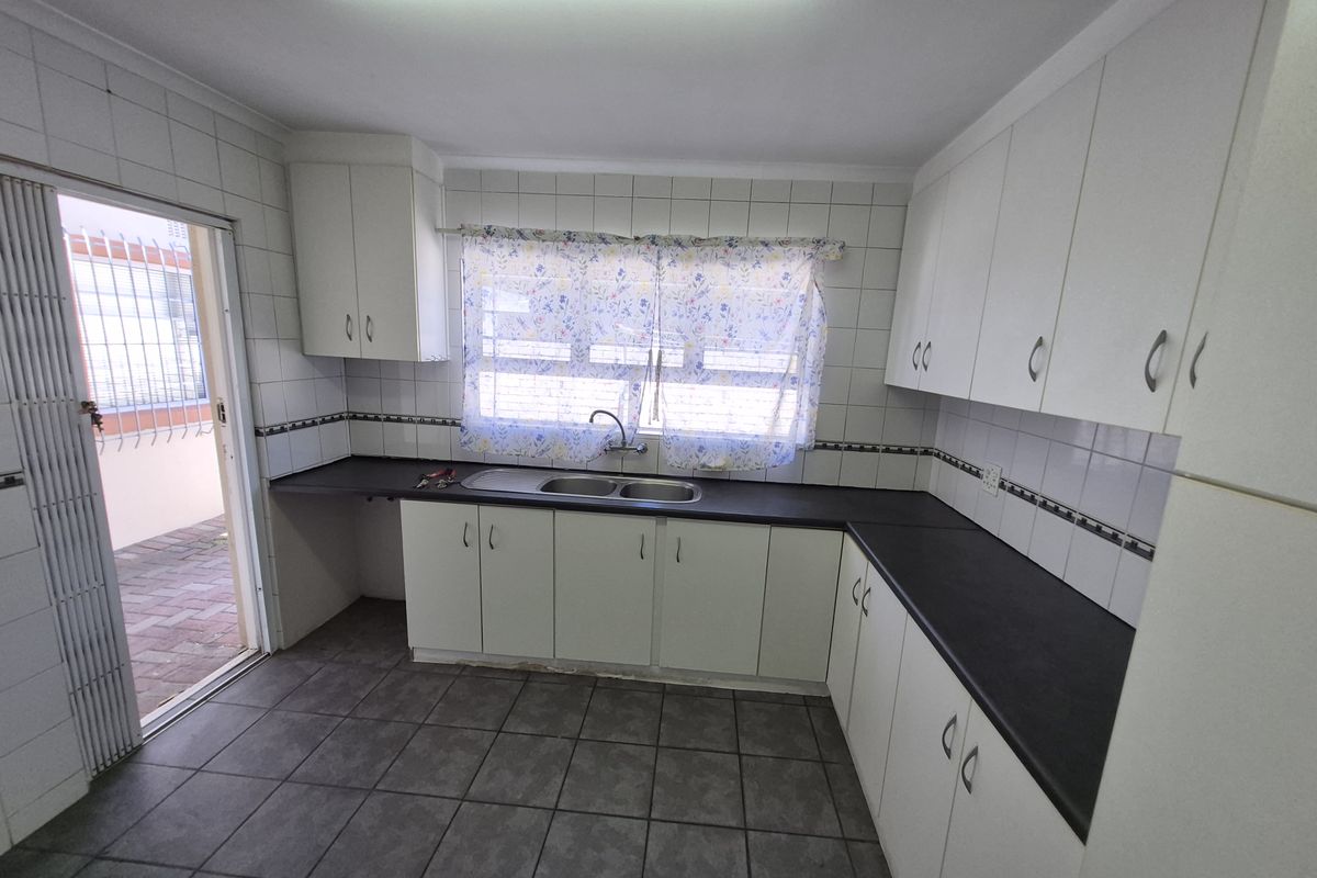 A functional kitchen featuring white cabinetry, dark laminate countertops, tiled flooring, and direct access to an outdoor area.