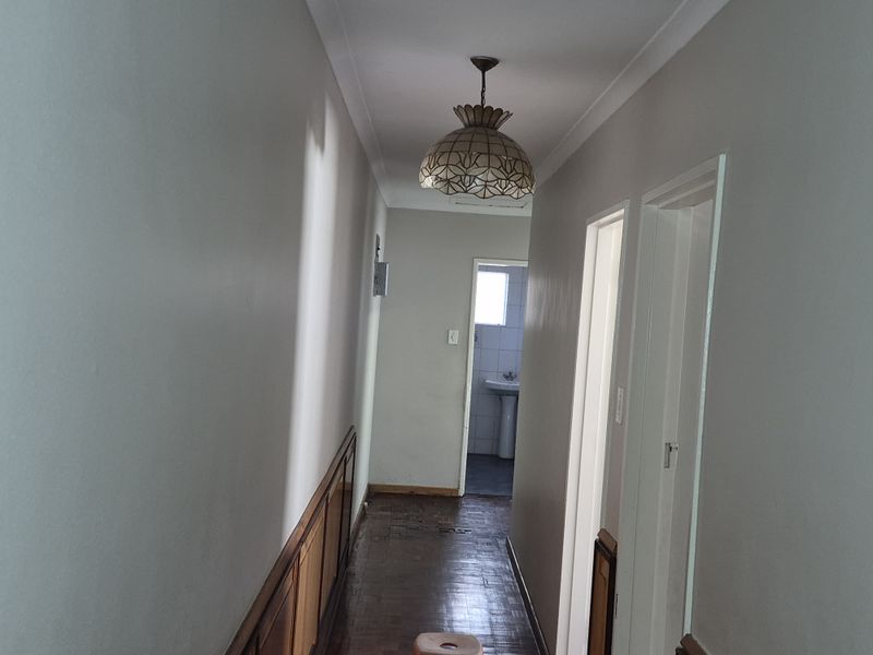 A functional hallway featuring classic parquet flooring and wooden wainscoting, providing access to adjacent rooms including a bathroom.