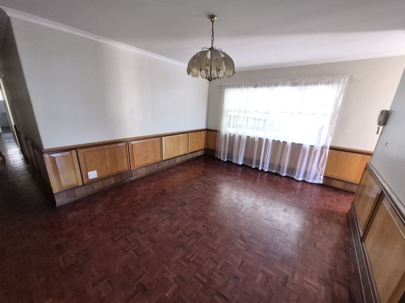 An empty living room featuring classic parquet flooring and traditional wooden wall paneling, offering a blank canvas for interior design updates.