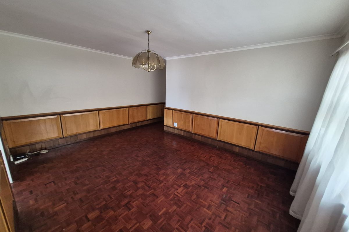 An empty living room featuring classic parquet flooring and built-in wooden wall paneling, offering a dated but solid foundation for renovation.