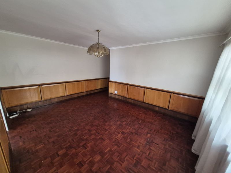 An empty living room featuring classic parquet flooring and built-in wooden wall paneling, offering a dated but solid foundation for renovation.