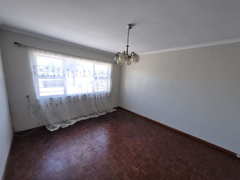 An empty living room featuring traditional parquet flooring, a central chandelier, and large windows fitted with security bars.