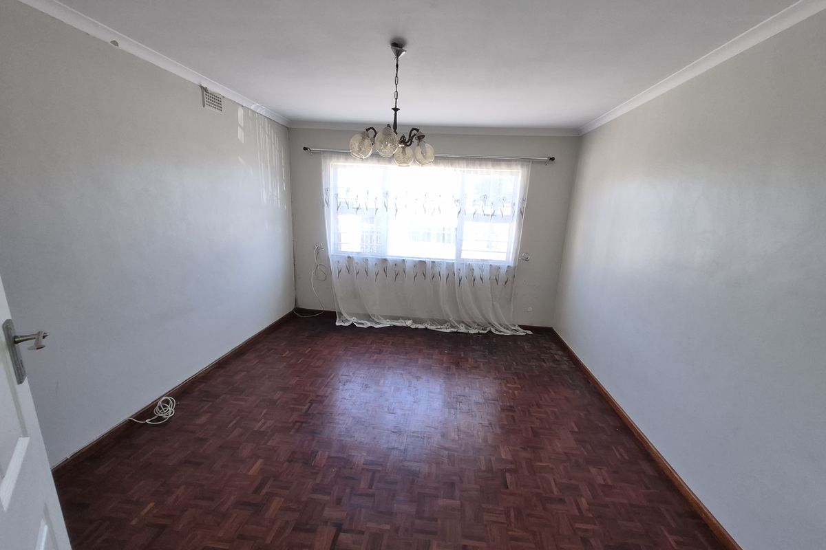An empty bedroom featuring original parquet flooring, cove cornicing, and a central ceiling light fixture, ready for renovation or staging.