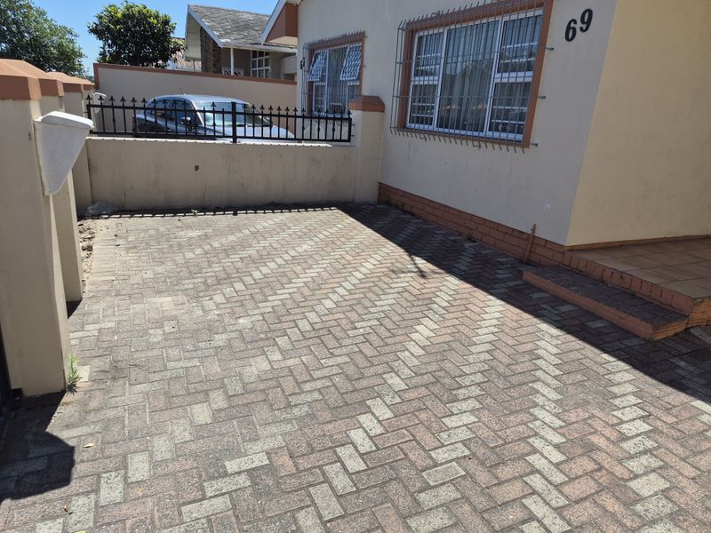 Front exterior view of a townhouse featuring a paved driveway, boundary wall with security fencing, and security bars on the windows.