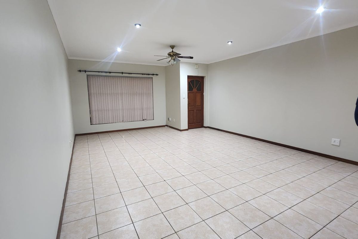 A spacious, empty living area featuring neutral tiled flooring, recessed downlighting, a ceiling fan, and a timber entrance door.