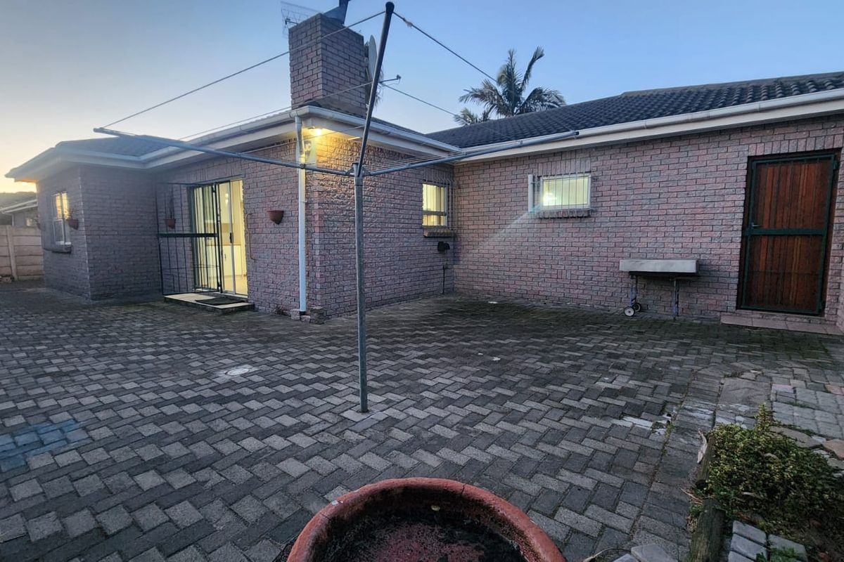 Rear exterior view of the house featuring a paved courtyard, brick facade, chimney, and sliding door access.