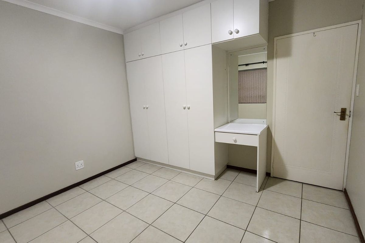A clean, empty bedroom featuring neutral tiled flooring and extensive white built-in cupboards with an integrated vanity area.