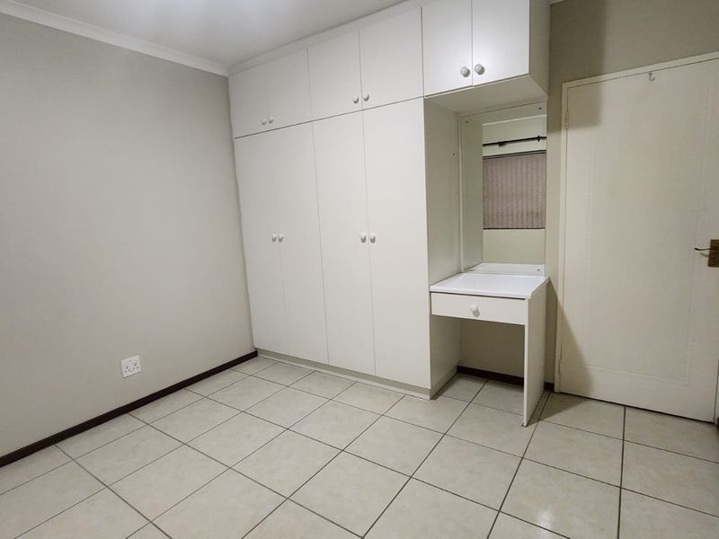 A clean, empty bedroom featuring neutral tiled flooring and extensive white built-in cupboards with an integrated vanity area.