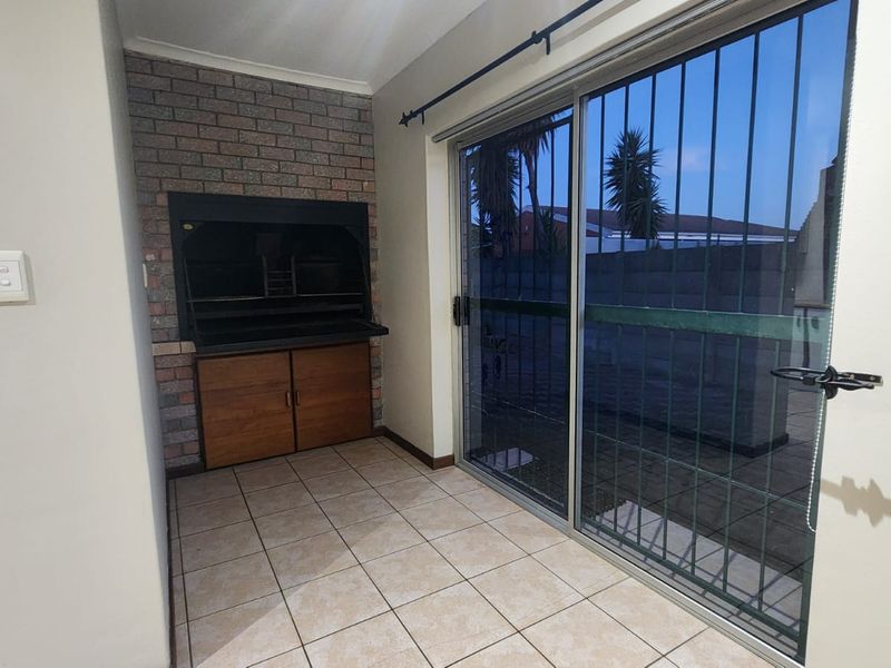 An indoor patio area featuring a built-in braai, tiled flooring, and a sliding glass door with security bars leading to the exterior.