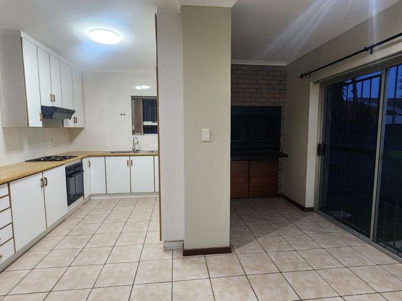 Open-plan kitchen and living area featuring tiled floors, built-in cabinetry, integrated appliances, and an indoor braai with direct access to the outdoor area.