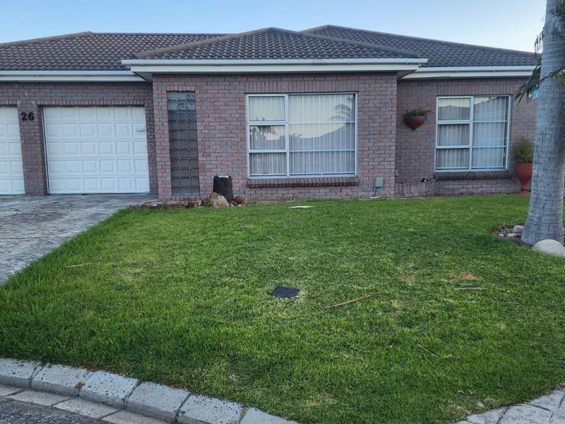 Front elevation of a single-story brick house featuring a tiled roof, paved driveway, and a well-maintained front lawn.