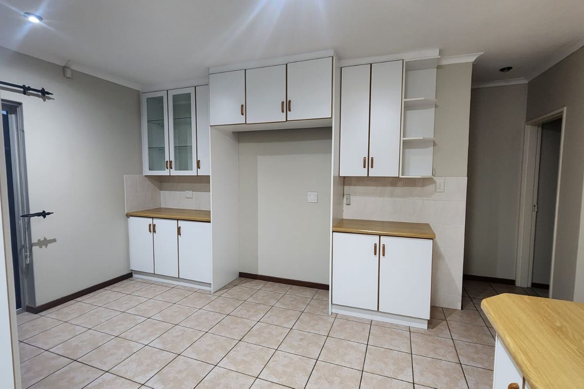 A clean, empty kitchen featuring white built-in cabinetry, laminate countertops, and neutral tiled flooring, offering a functional space ready for personalization.